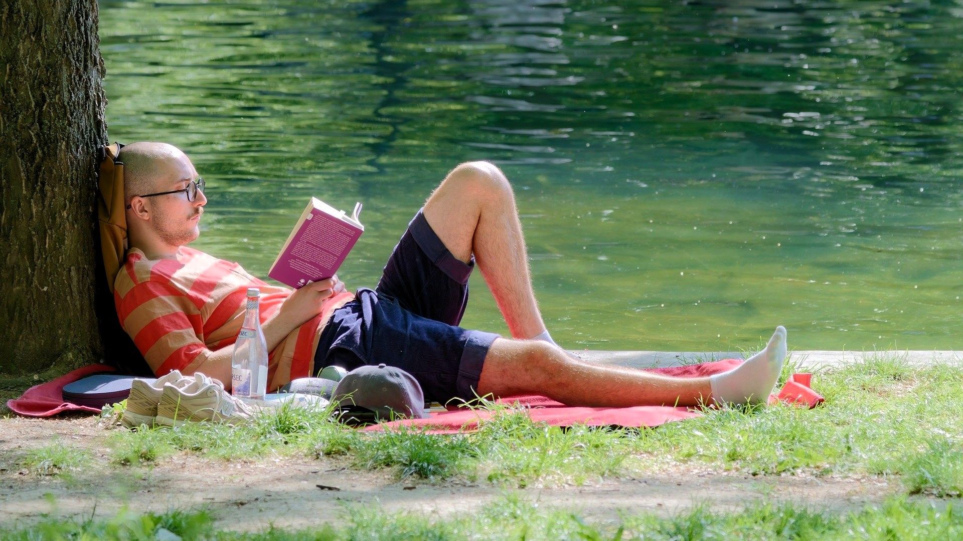 Hombre relajado leyendo un libro junto a un lago, símbolo de abundancia consciente