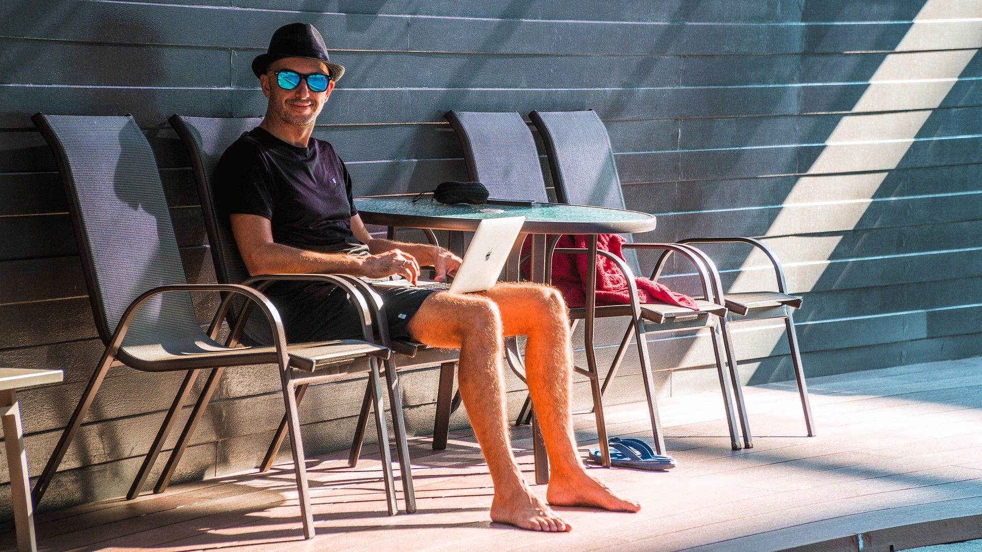 Hombre relajado con portátil, descalzo en una terraza soleada, simbolizando equilibrio digital.