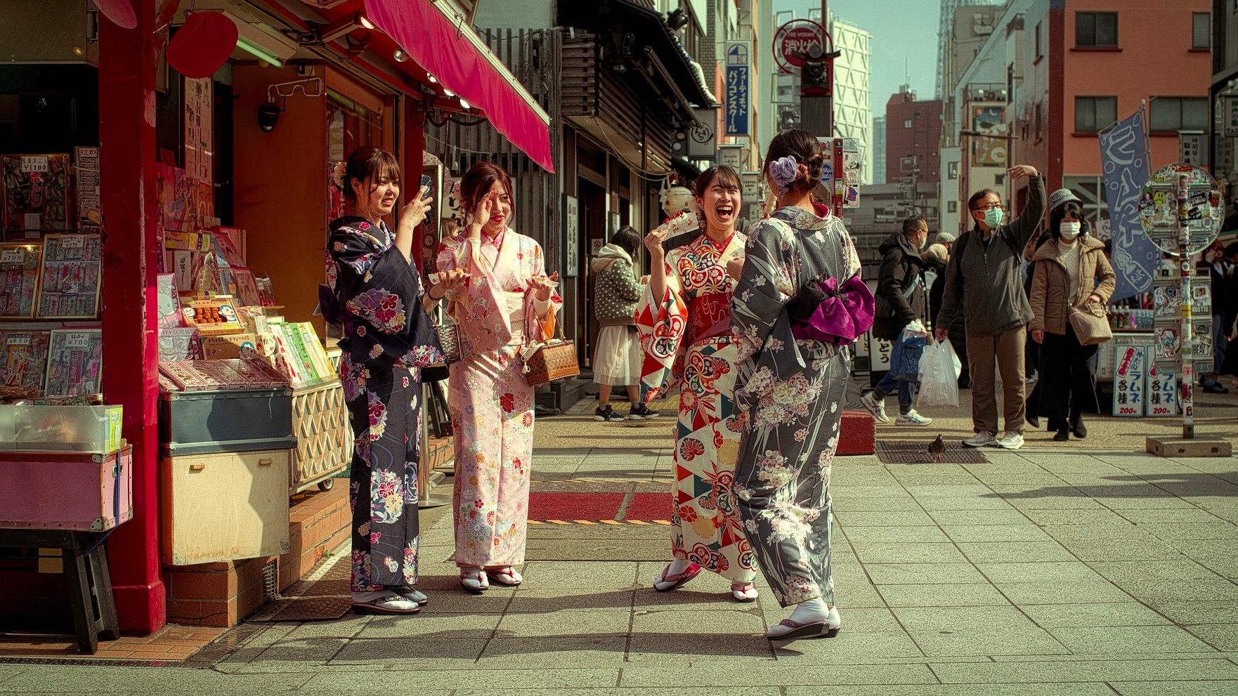 Cuatro mujeres japonesas con kimonos ríen y comparten un momento frente a una tienda en una calle de Tokio
