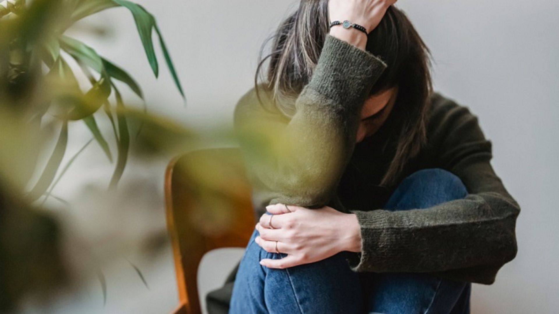 Mujer con gesto de ansiedad sentada con los brazos sobre las piernas, en interior, simbolizando estrés y necesidad de calma