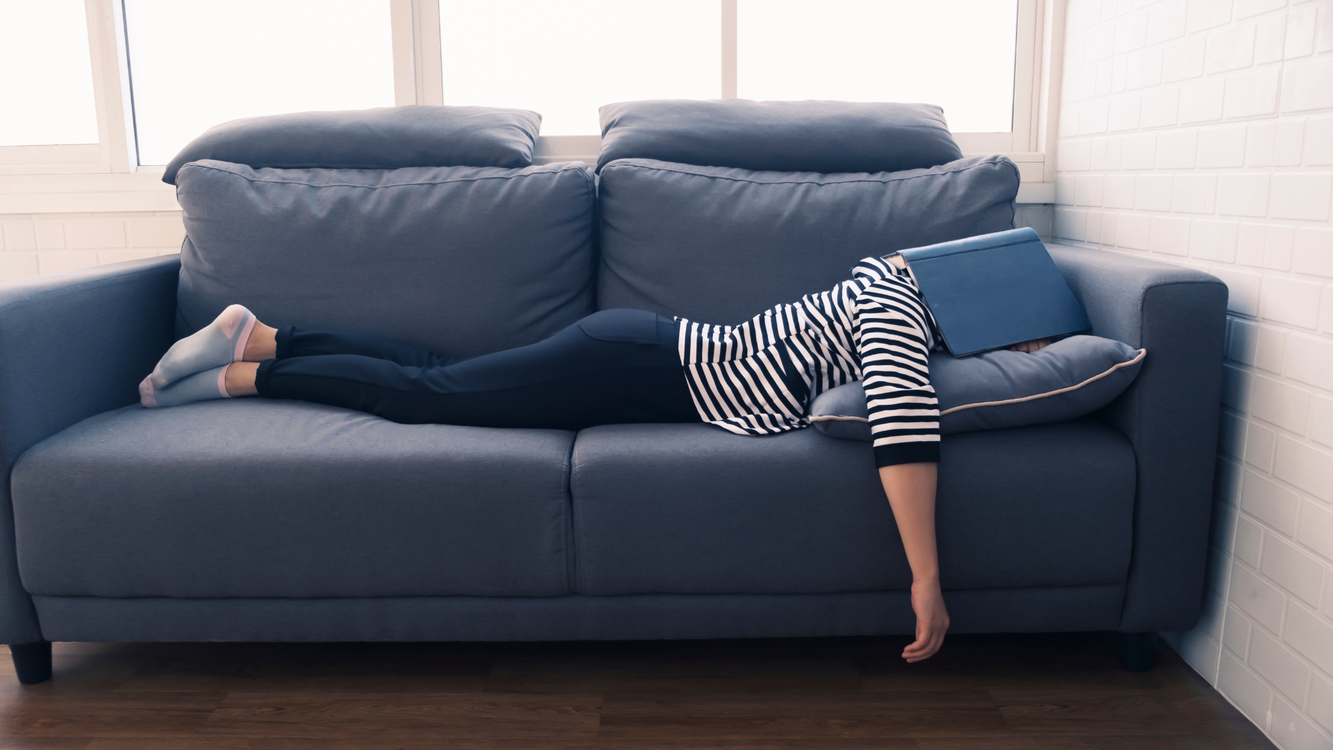 Persona tumbada en el sofá con un portátil sobre la cara, símbolo de procrastinación y cansancio mental